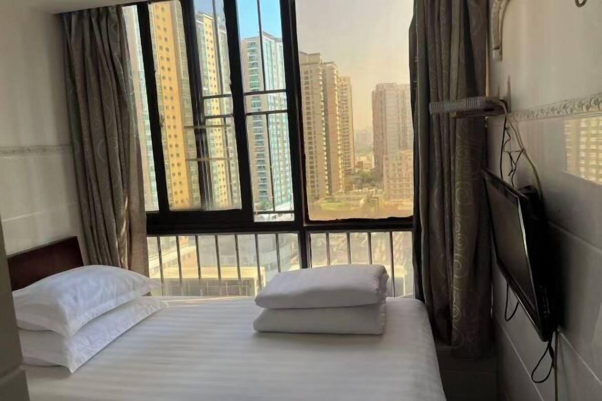 Habitación de hotel con cama, cortinas, ventana que ofrece vistas de edificios altos y un televisor de pared.