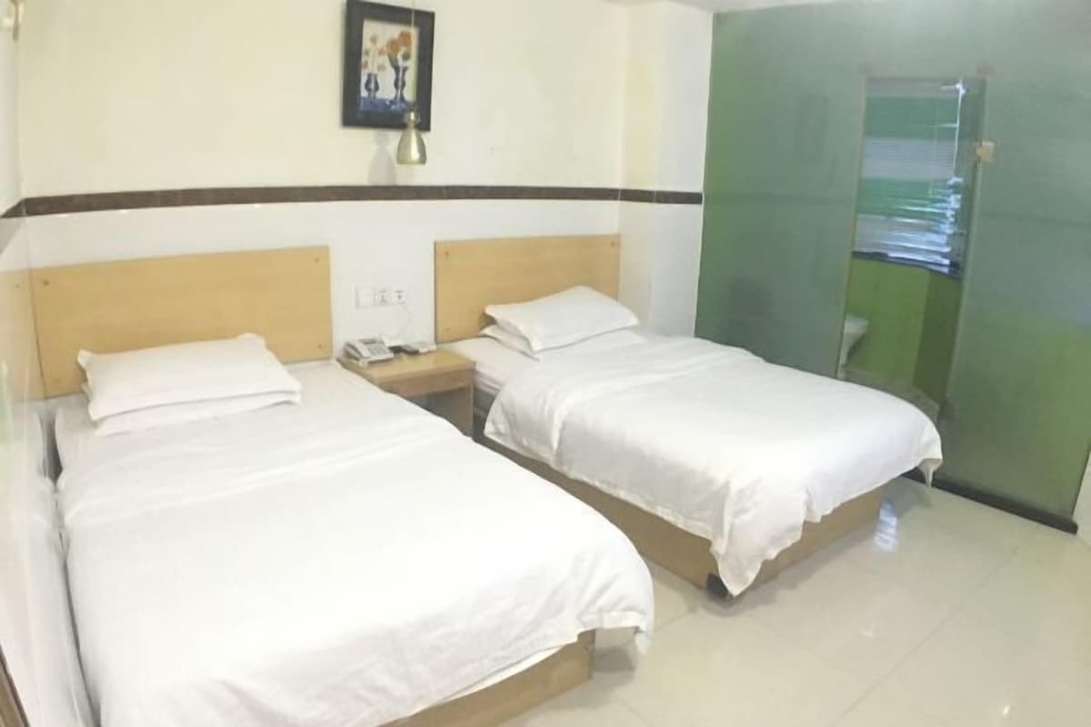 A hotel room with two single beds, a nightstand with a phone, a framed picture on the wall, and a green door.