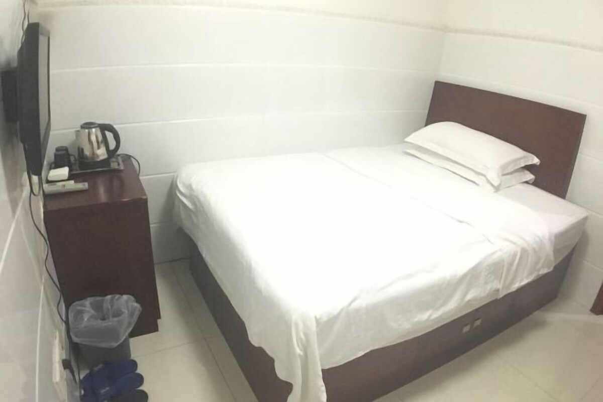 A small, clean room with a bed, a nightstand, a TV, and a trash bin.