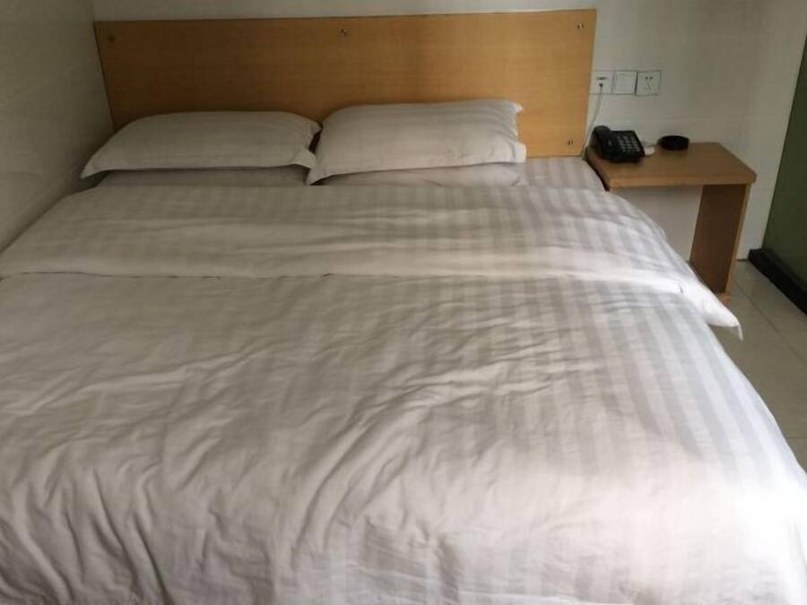 Un llit ben fet amb capçalera de fusta, una taula de nit amb un telèfon i una presa corrent.