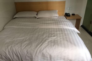 A neatly made bed with a wooden headboard, a bedside table with a phone, and a wall socket.