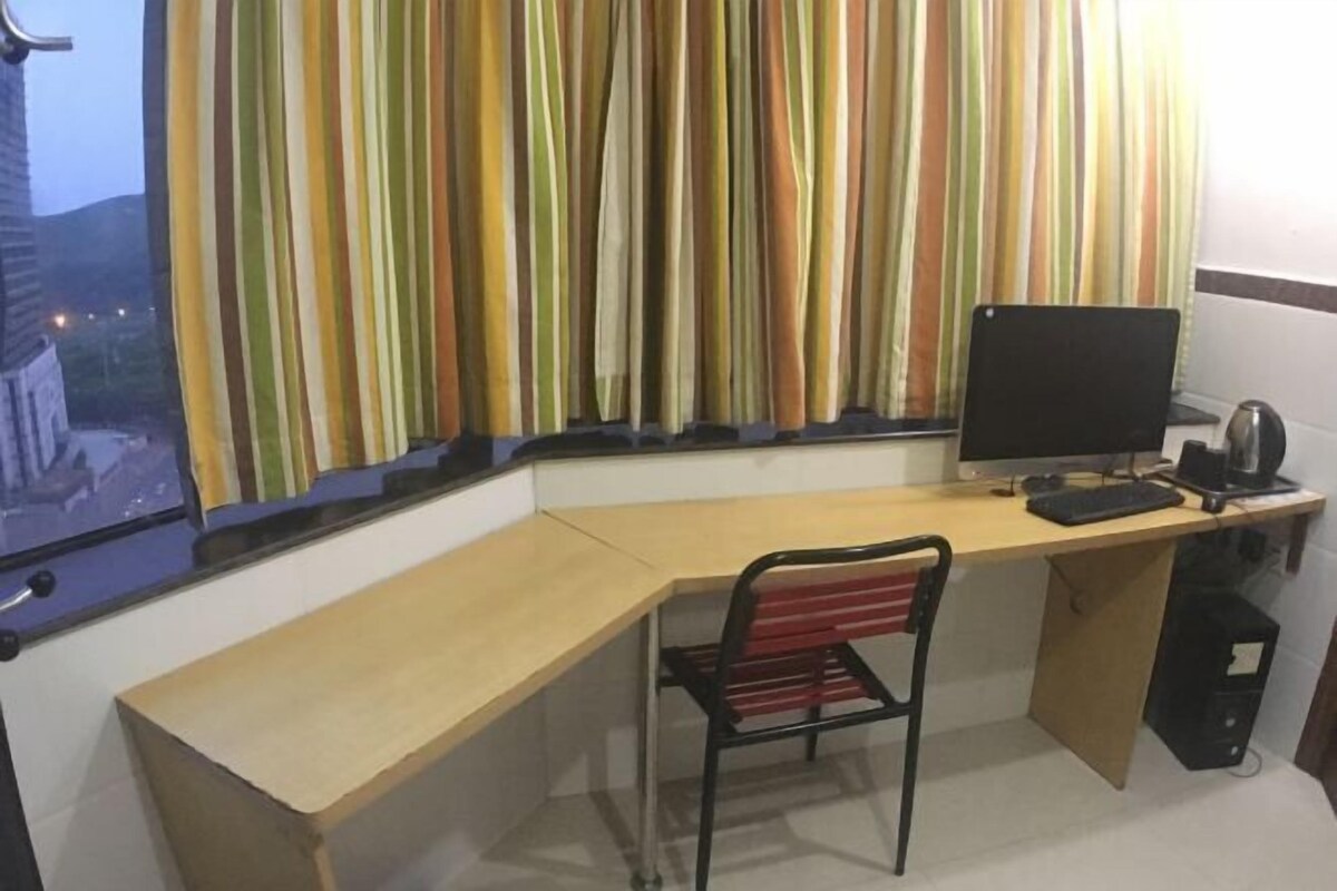 A corner room with a desk, a chair, a computer, and a window with striped curtains.