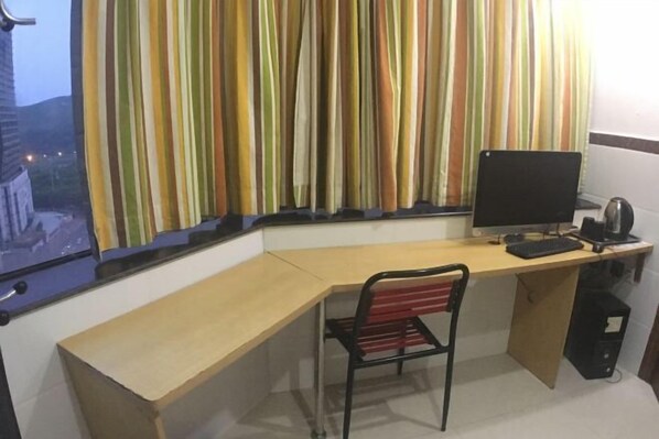 A corner room with a desk, a chair, a computer, and a window with striped curtains.