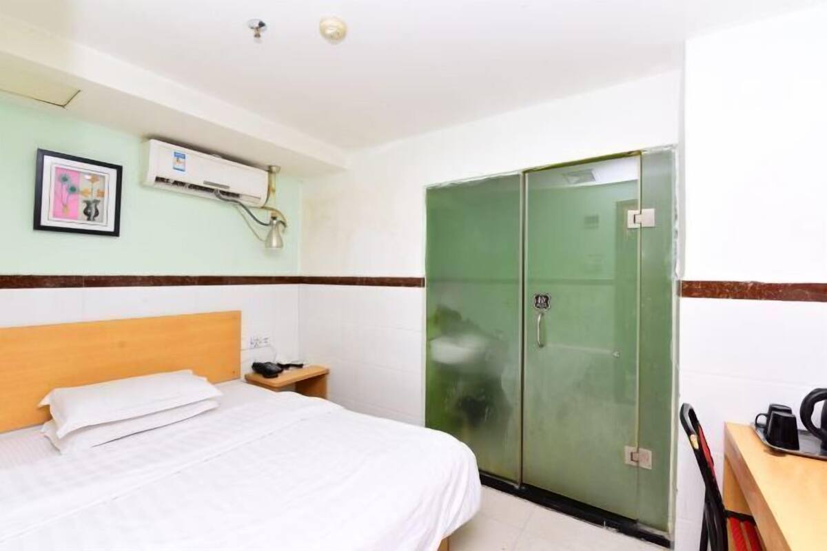 Habitación de hotel con cama, un armario verde, una mesita de noche con lámpara y un aire acondicionado de pared.