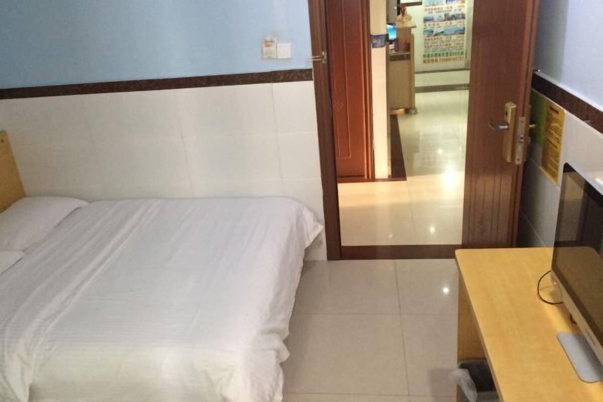 Una habitación de hotel con cama, un escritorio con computadora y una puerta que da a un pasillo.