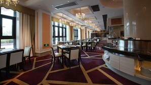 Une salle à manger d’hôtel avec de nombreuses tables et chaises, un buffet et de grandes fenêtres laissant entrer la lumière naturelle.
