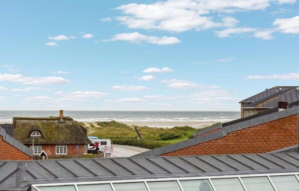 Uitzicht op de kust met een huis met rieten dak, een gebouw van baksteen en een caravan langs een weg.
