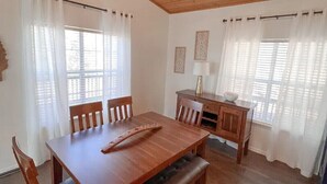 A dining area with a wooden table and chairs, a bench, a small cabinet, and two windows with sheer curtains. - PERFECT GETAWAY cabin near Turner Falls & Lake of The Arbuckles. (Sulphur)