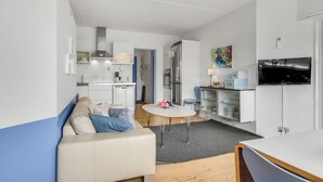 Un espacio habitable compacto con kitchenette, comedor, sofá, televisor y un cuadro.