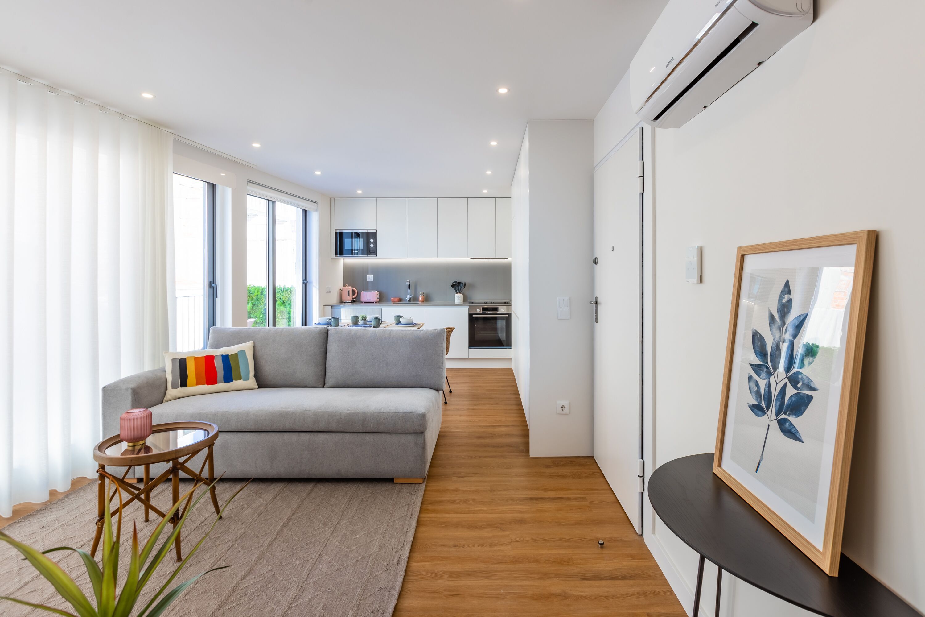 Een moderne woonkamer met een grijze bank, een klein rond tafeltje en een lijstwerk kunstwerk aan de muur.