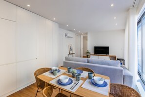 Un salon moderne comprenant un coin repas, un canapé gris, un téléviseur à écran plat et de grandes fenêtres.