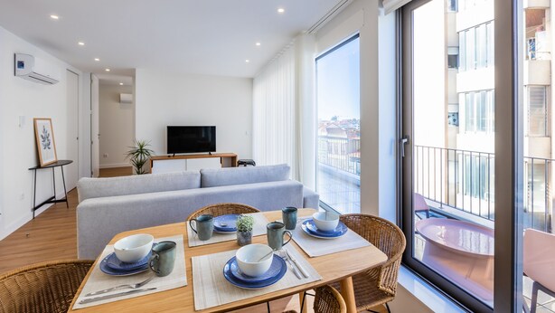 A modern living room with a sofa, dining table, and a balcony with a view of the city. - Pestana Apartments T1 Terrace  (Porto)
