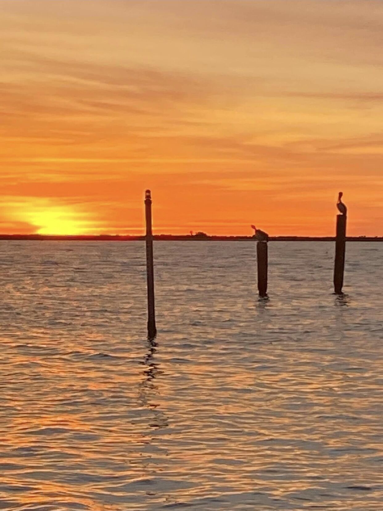Un atardecer sobre una masa de agua tranquila con tres postes verticales en primer plano.