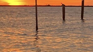 Un atardecer sobre una masa de agua tranquila con tres postes verticales en primer plano.