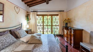A bedroom with a large bed, a wooden dresser, a nightstand, and a window with a view of greenery.