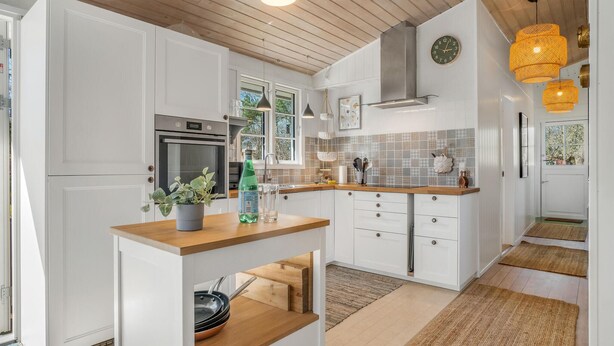 Una cocina moderna con armarios blancos, encimera de madera y horno empotrado.