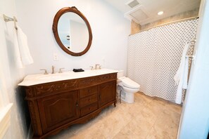 A bathroom with a wooden vanity, a round mirror, a white toilet, and a shower curtain with a pattern. - Charming Historic Home with chef's kitchen formal dining, sitting room, & patio (Payson)