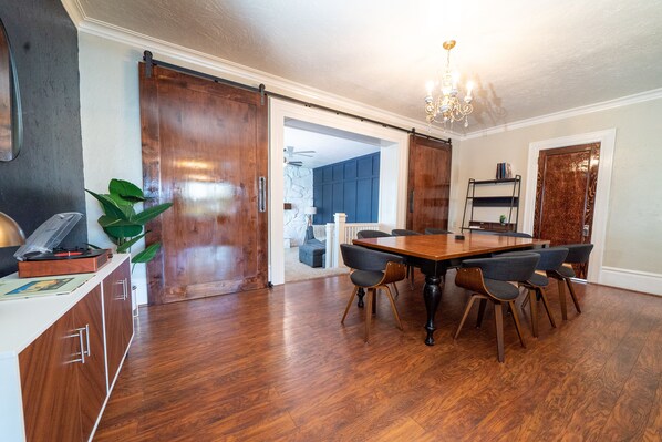 A dining area with a wooden table and chairs, a chandelier, and a sliding door leading to another room. - Charming Historic Home with chef's kitchen formal dining, sitting room, & patio (Payson)
