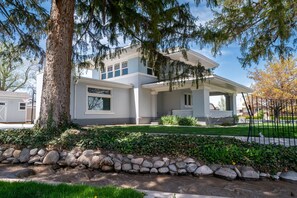 A modern two-story house with a stone retaining wall, a covered porch, and a well-maintained lawn. - Charming Historic Home with chef's kitchen formal dining, sitting room, & patio (Payson)