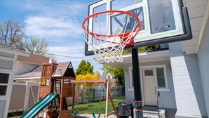 A basketball hoop attached to a house with a white exterior and a wooden play structure nearby. - Charming Historic Home with chef's kitchen formal dining, sitting room, & patio (Payson)