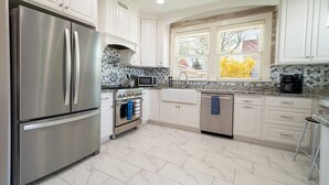 A modern kitchen with stainless steel appliances, white cabinetry, and a window with blinds. - Charming Historic Home with chef's kitchen formal dining, sitting room, & patio (Payson)