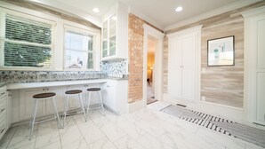 A kitchen with white cabinets, a marble countertop, three bar stools, and a brick accent wall. - Charming Historic Home with chef's kitchen formal dining, sitting room, & patio (Payson)