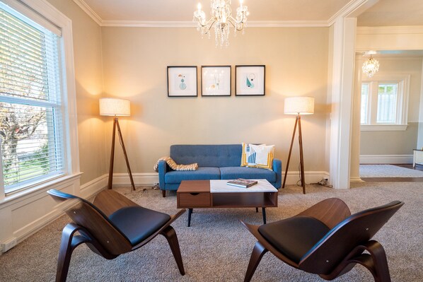 A living room with a blue sofa, two armchairs, a coffee table, and three framed artworks on the wall. - Charming Historic Home with chef's kitchen formal dining, sitting room, & patio (Payson)