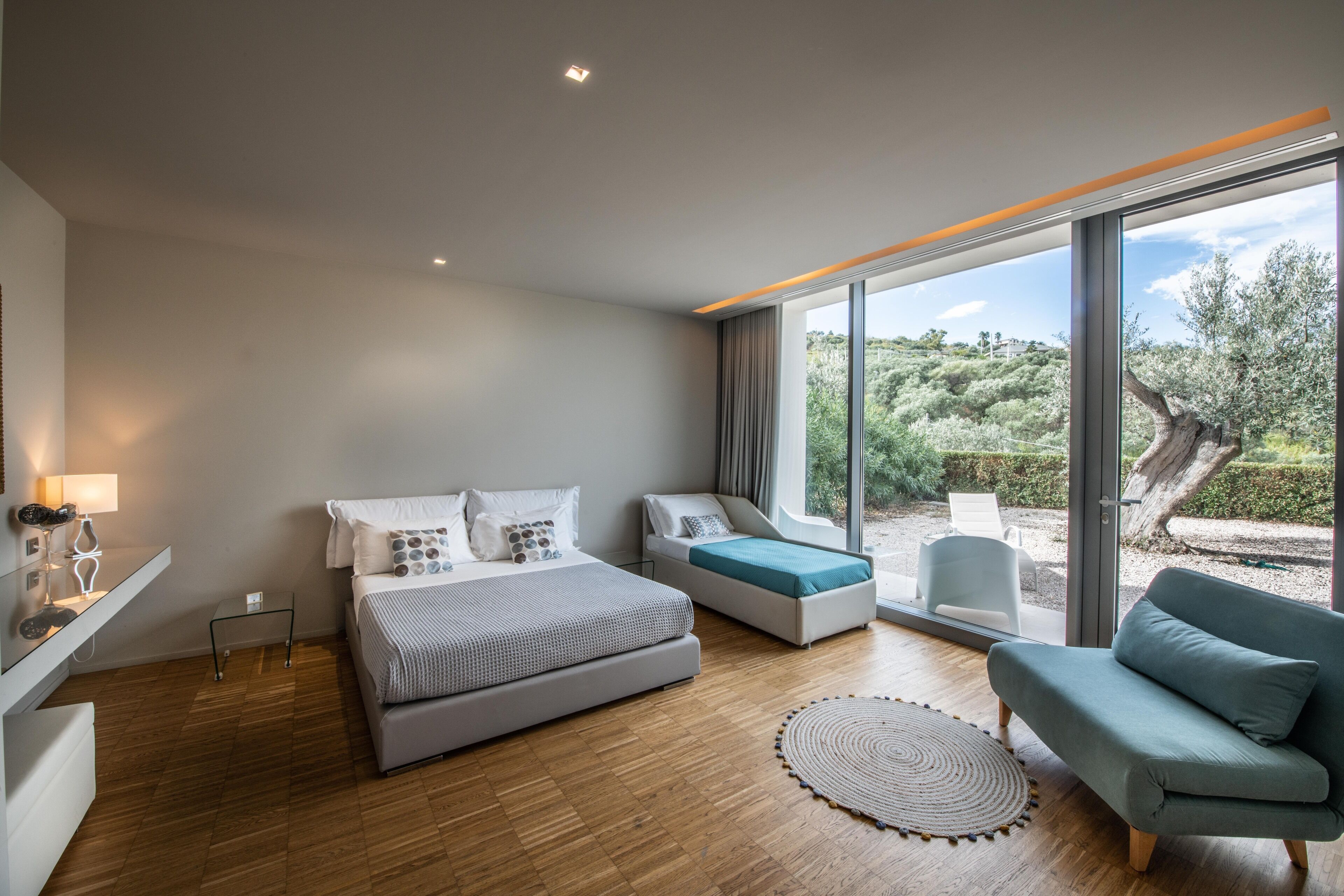A modern bedroom with a large bed, a sofa, and a view of a garden.