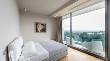 Un dormitorio moderno con una cama grande, vistas a la ciudad a través de ventanales y un diseño minimalista.
