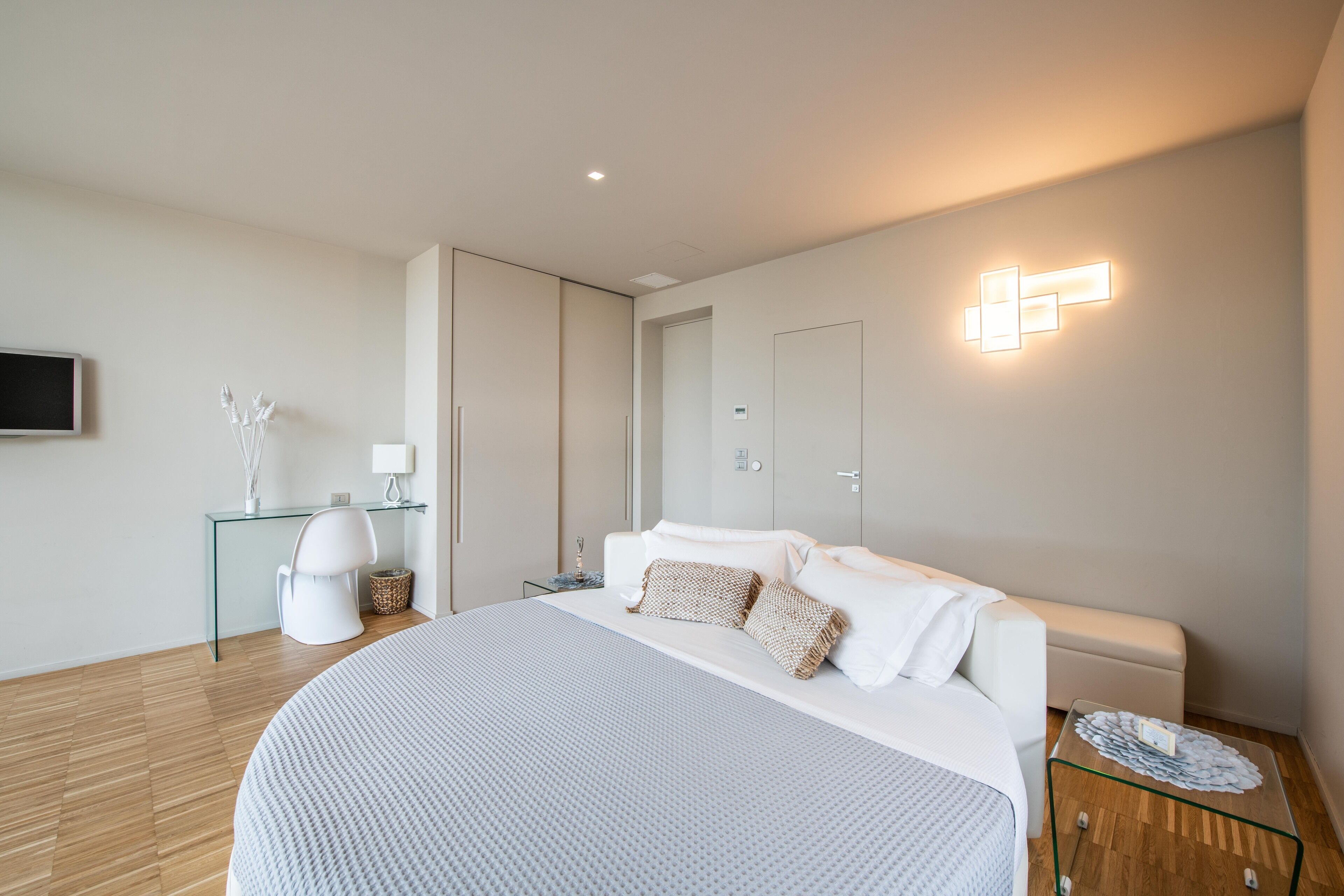 Ein modernes Schlafzimmer mit einem großen Bett, Nachttischen, einem Schreibtisch und einem an der Wand befestigten Fernseher.