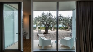 Une chambre moderne dotée d’une grande porte-fenêtre coulissante qui donne sur un espace extérieur aménagé avec deux chaises blanches et un arbre.