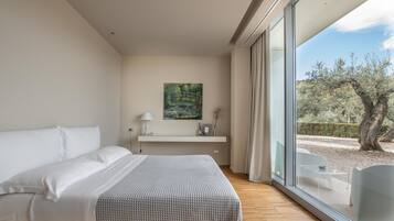 Un dormitorio moderno con una cama grande, una mesita de noche con lámpara, un cuadro y vistas a un jardín exterior a través de un ventanal.