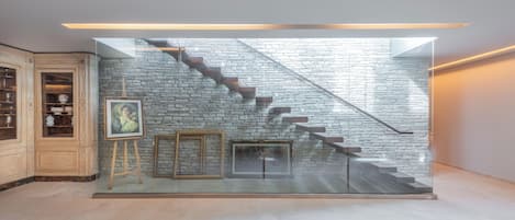 A modern interior with a glass staircase against a stone wall, wooden cabinets, and framed artwork.