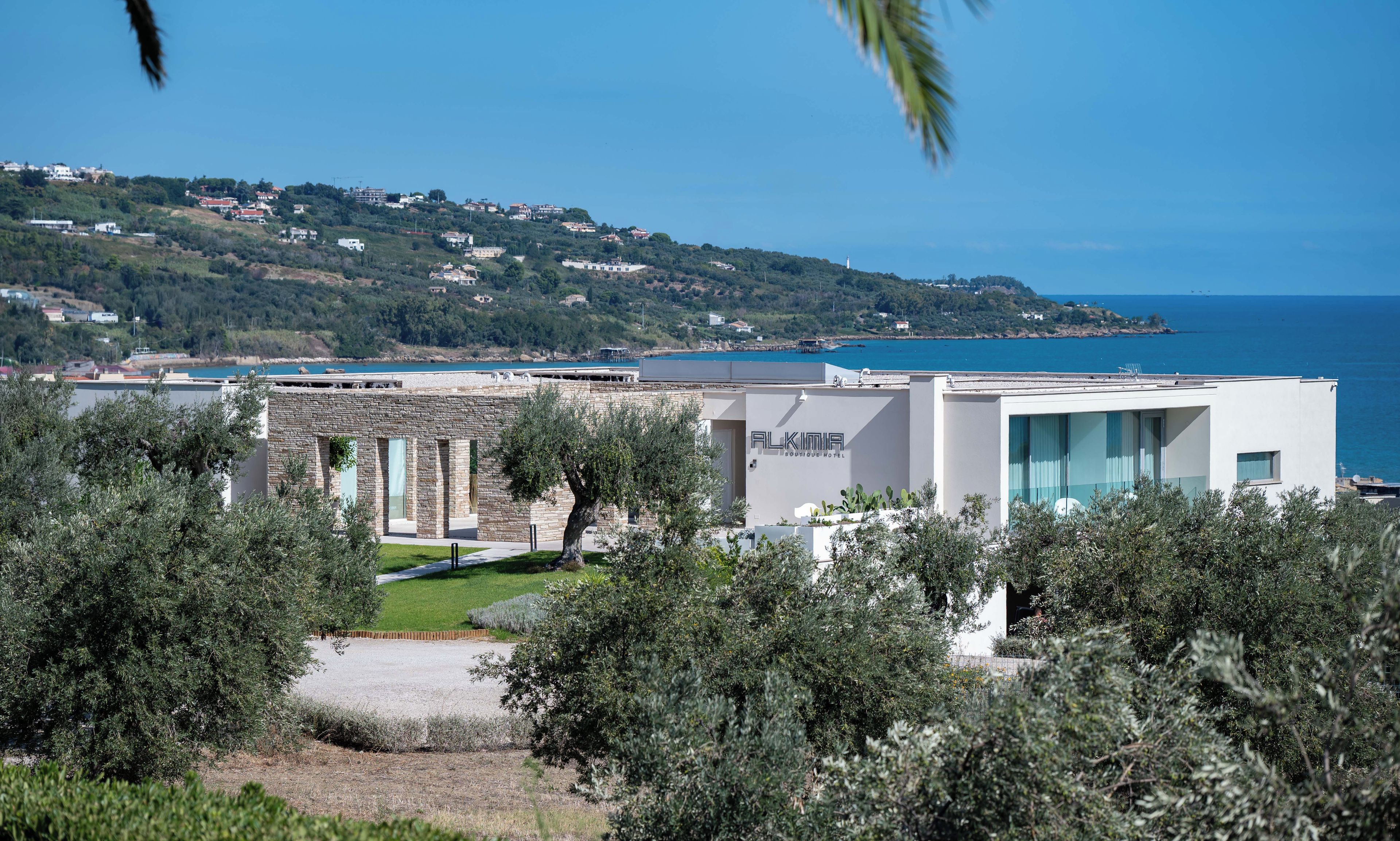Ein modernes Hotel mit Blick auf das Meer und eine hügelige Landschaft im Hintergrund.