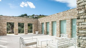 Une terrasse extérieure moderne, avec des meubles blancs, des murs en pierre et un ciel dégagé.