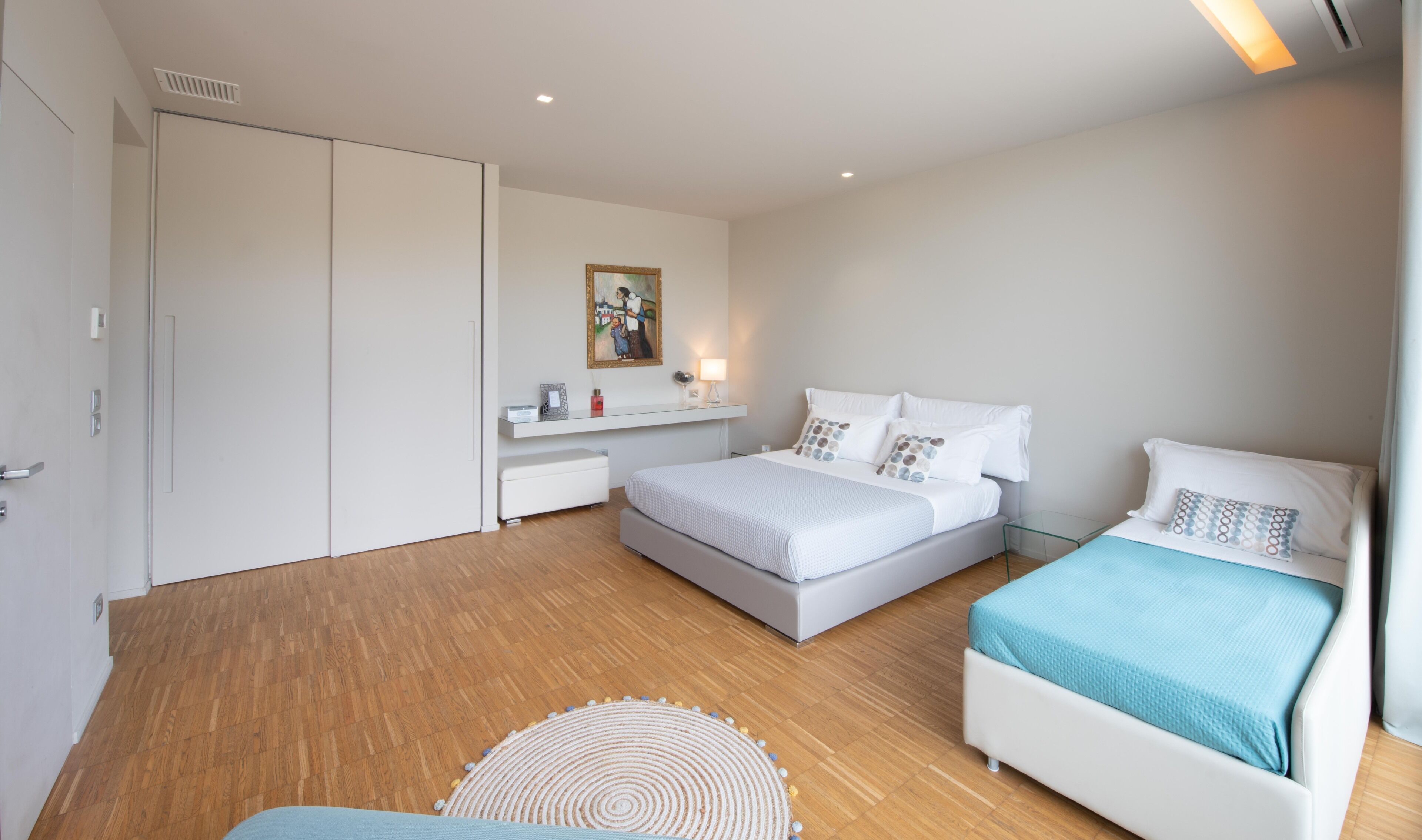 Een moderne slaapkamer met een groot bed, een klein bed, een bureau en een kledingkast.
