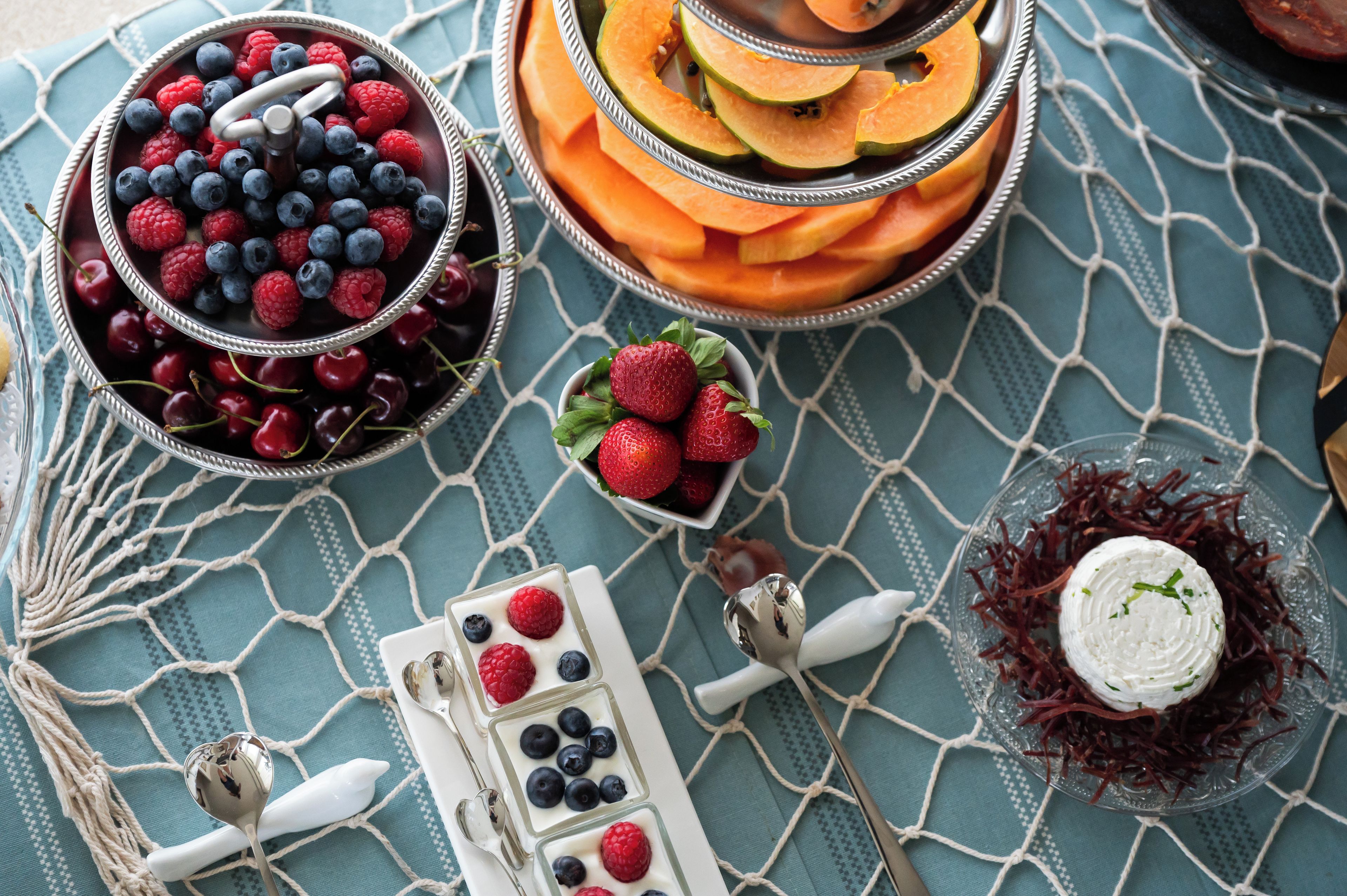 A variety of fruits and a dessert on a table with a blue patterned tablecloth.