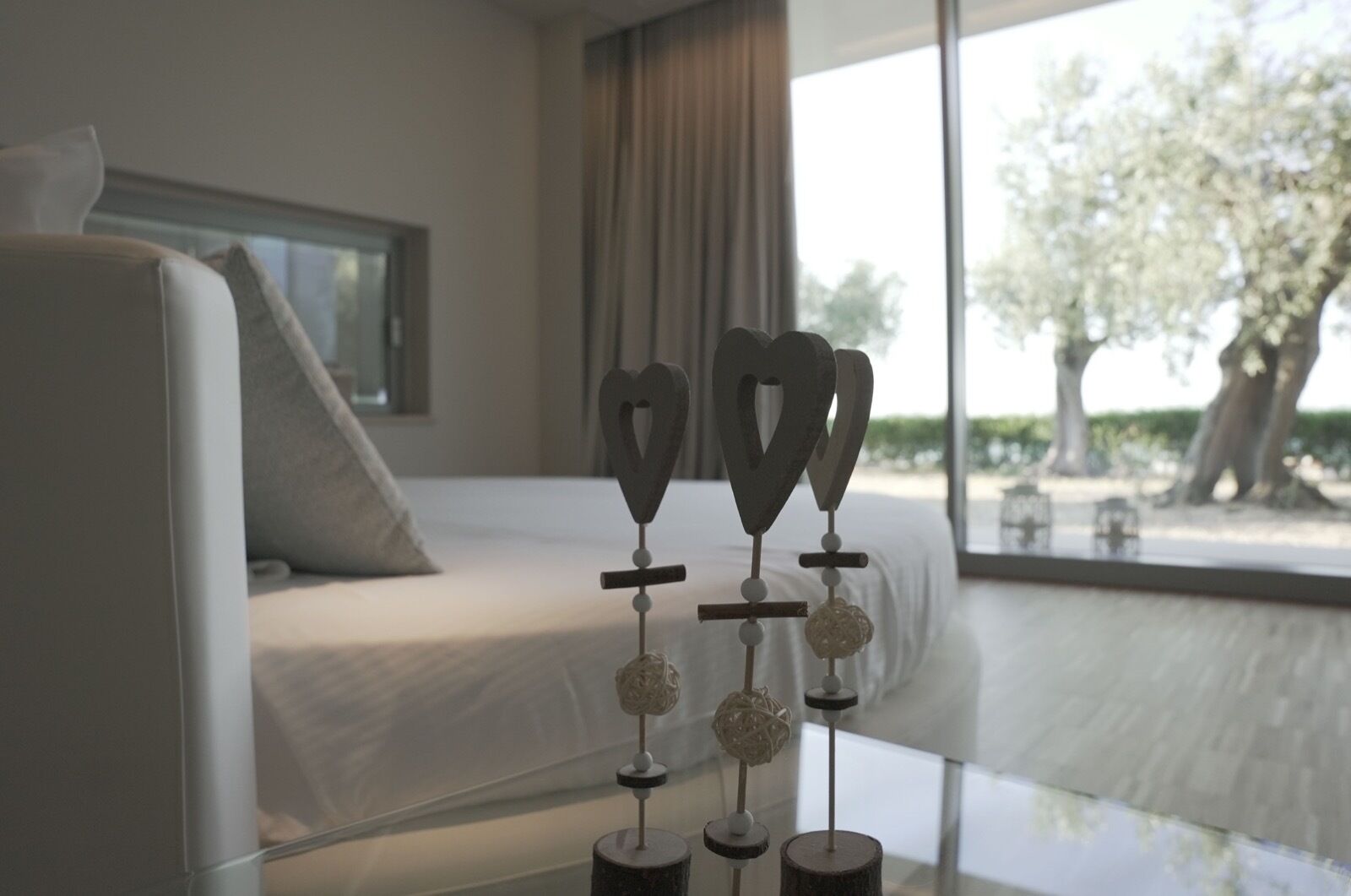 Una habitación de hotel moderna con una cama, una mesita de vidrio y vistas a árboles.