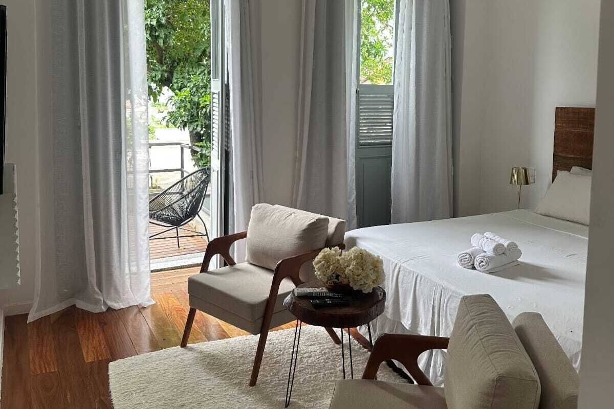 A bedroom with a bed, two chairs, a small table with flowers, and a hanging light fixture.
