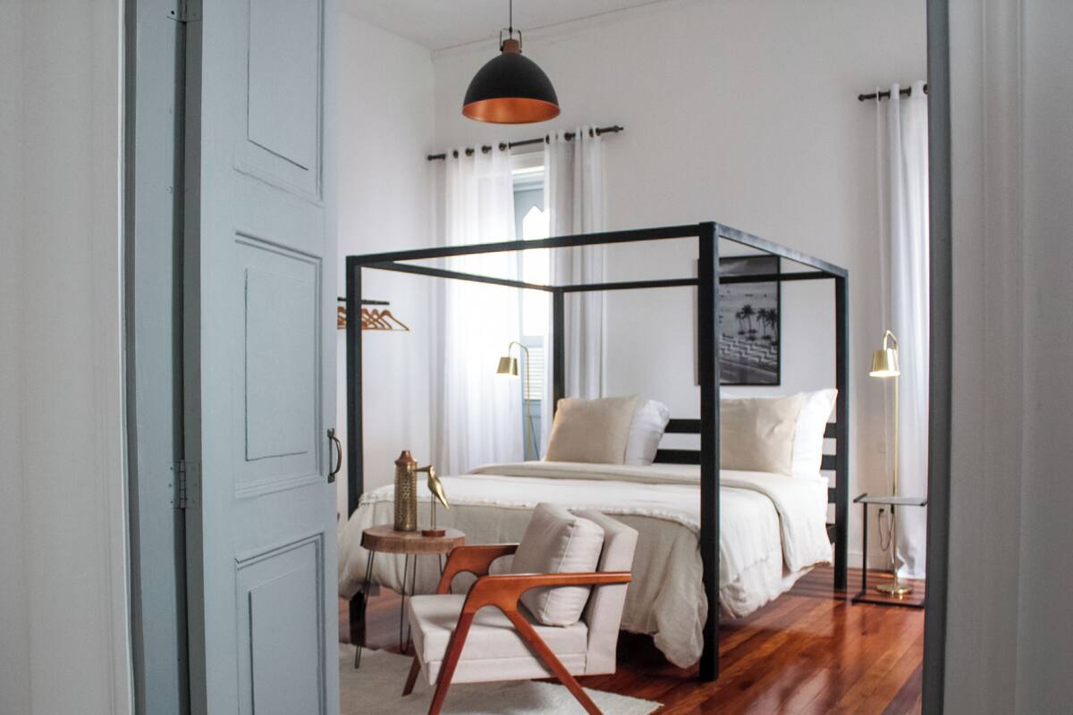 A modern bedroom with a four-poster bed, a small side table, a chair, and a floor lamp.