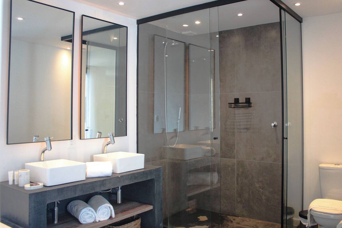 A modern bathroom with two sinks, a glass shower enclosure, and a toilet.