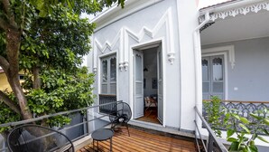 A balcony with wooden flooring and two black chairs, a white building with decorative trim, and a tree in the background. - Boutique Hotel Castelinho (Rio de Janeiro)