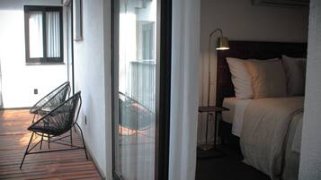 A room with a bed, a chair, a lamp, and a view of the outside balcony.