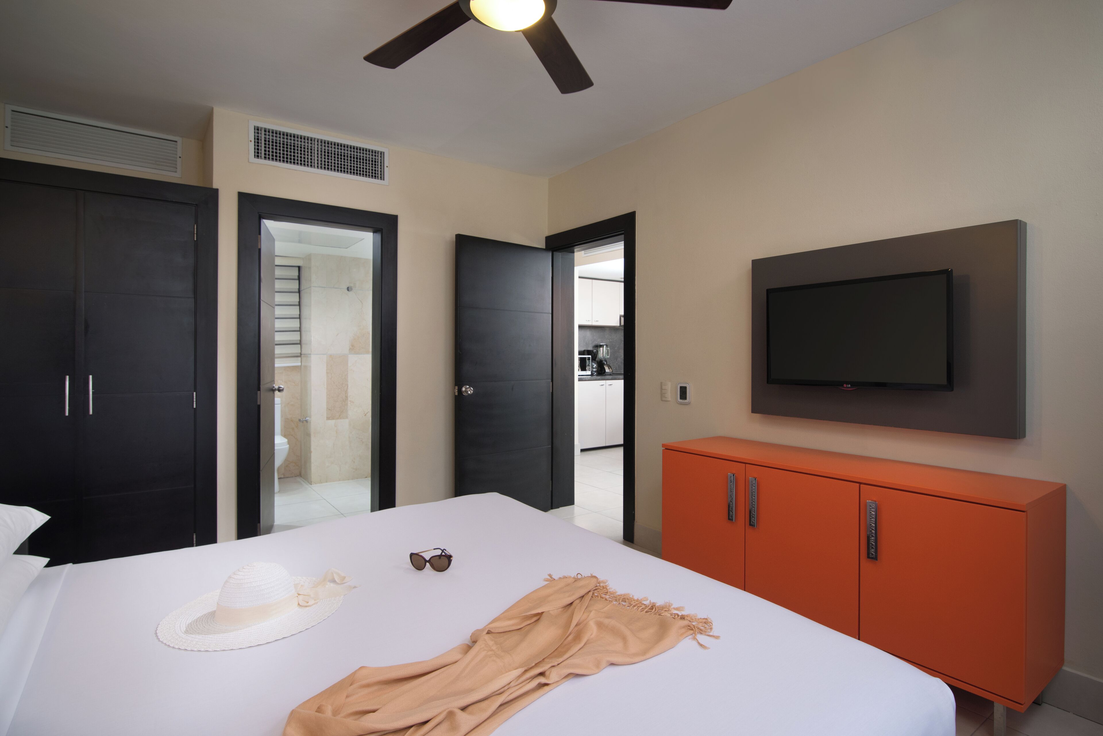 A hotel room with a bed, a TV mounted on the wall, a wardrobe, and a ceiling fan.