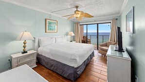 A hotel room with a bed, bedside tables, a desk, a chair, a ceiling fan, and a view of the ocean. - The Summit 1503 (Panama City Beach)