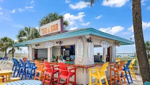 Un bar de style tiki avec des chaises et des tables aux couleurs vives, une enseigne et un panneau affichant le menu.