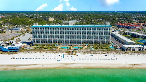 Un grand hôtel à plusieurs étages, doté d’une piscine et d’un espace de plage aménagé avec des parasols.