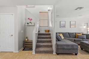 A modern living room with a grey sectional sofa, a staircase with a patterned carpet, and a white door.