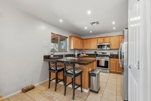 A modern kitchen with a central island, wooden cabinets, stainless steel appliances, and a tiled floor.