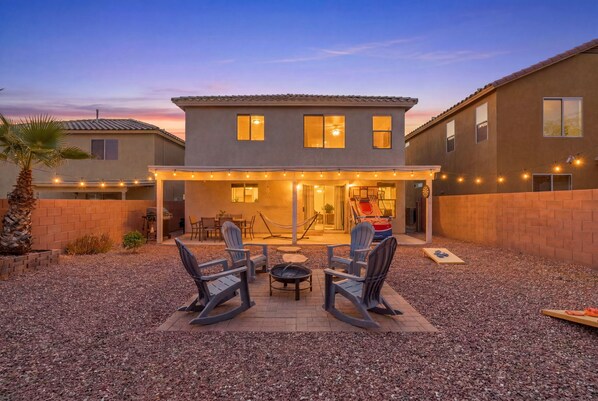 A two-story house with a covered patio area featuring outdoor furniture and string lights.
